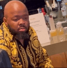 a bald man with a beard is wearing a yellow shirt and sitting at a table .