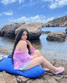 a woman sits on a blue pillow near the water