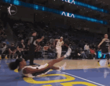 a female basketball player is laying on the floor during a game with the letters ala visible in the background