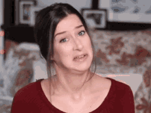 a woman in a red shirt is making a funny face and looking at the camera .