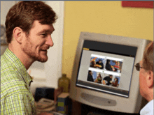 a man in a green plaid shirt looks at a computer screen with pictures on it