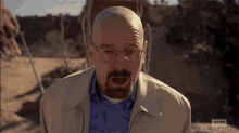 a bald man with a beard and glasses is making a funny face while standing in the desert .