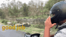 a man wearing a helmet talks on a cell phone while riding a motorcycle with the words " good job " behind him