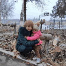 a little girl is being held by a woman in front of a fence with a sign that says ' a ' on it