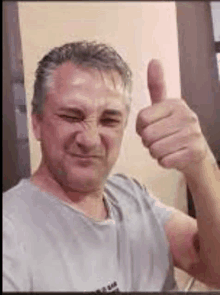 a man is giving a thumbs up sign while wearing a gray shirt .