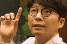 a man wearing glasses is pointing up with his finger