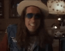 a man with long hair is wearing a hat and sunglasses .