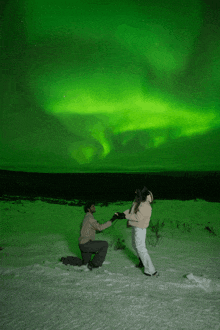 a man kneels down to propose to a woman under a green aurora borealis