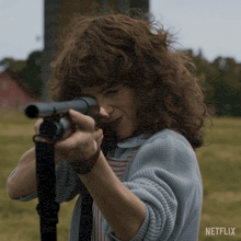 a woman with curly hair is pointing a shotgun at the camera with a netflix logo behind her