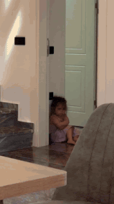 a little girl in a pink dress sits on the floor in front of a door
