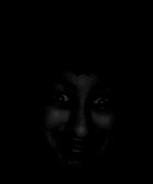 a black and white photo of a woman 's face in the dark with glowing eyes .