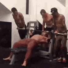 a group of men are standing around a man lifting weights in a gym .