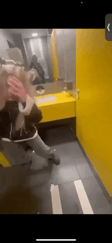 a woman is standing in a public restroom covering her face with her hands .