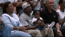 a group of people are sitting in a stadium watching a game and one man is holding a baby