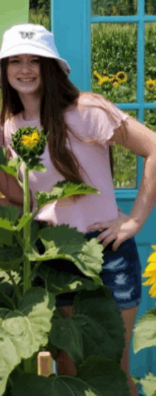 a girl wearing a white hat with a butterfly on it is standing next to a sunflower