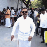 a man wearing sunglasses and a white shirt is standing in front of a crowd of people