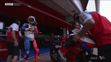 a motorcycle racer wearing a ducati outfit is being helped by a mechanic