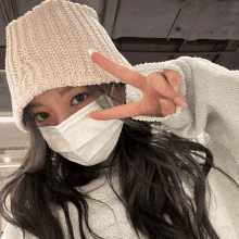 a woman wearing a mask and a beanie is giving the peace sign