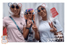 three women wearing wigs and sunglasses pose for a photo in front of a sign that says south olympic games