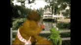 a teddy bear and a kermit the frog are standing next to each other in front of a fence .