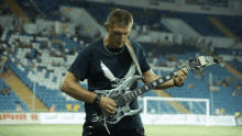 a man playing a guitar in front of a stadium with a sign that says ' army b '