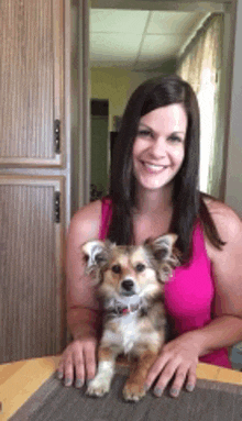 a woman is sitting at a table holding a small dog .