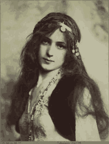 a black and white photo of a woman with long hair wearing a headband and a vest .