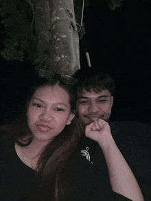 a man and a woman are posing for a picture with a tree behind them