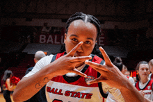 a woman wearing a ball state jersey making a peace sign with her hands