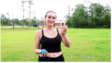 a woman in a black tank top is holding a blue ball and making a peace sign