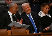 a man in a suit and tie smiles while sitting next to two other men