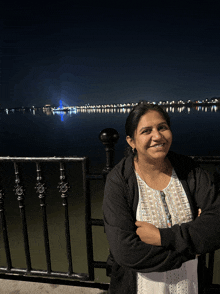 a woman stands with her arms crossed in front of a lake