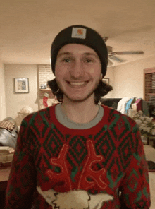 a man wearing a beanie and a christmas sweater smiles