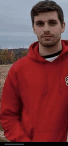 a young man wearing a red hoodie is standing in a field .