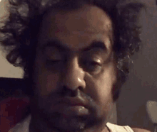 a man with curly hair and a beard is making a funny face .