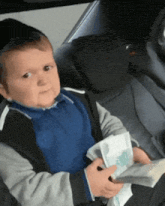 a baby is sitting in a car seat holding a piece of paper