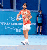 a man holding a tennis racquet on a tennis court with vitale barberis 1663 written on the wall behind him