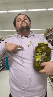 a man in a purple hoodie holds a jar of mt olive kosher dill pickles