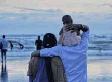 a man holds a baby on his shoulders while a woman looks on