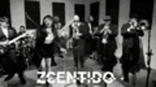 a black and white photo of a group of people dancing and singing in a room .