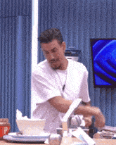 a man in a white shirt is standing in front of a table with plates and bowls on it .