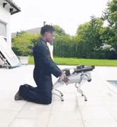 a man is kneeling down next to a robotic dog .