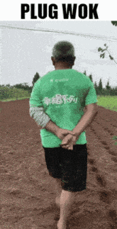 a man in a green shirt is walking barefoot on a dirt road with the words plug wok above him