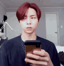 a man with red hair is taking a picture of himself in a mirror while holding a cell phone .