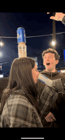 a man and a woman standing next to each other with a can of bud light on top of a stack of cans