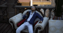 a man in a blue jacket and white pants is sitting in a white chair