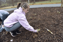 a girl wearing a pink sweatshirt is kneeling down in the dirt