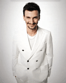 a man wearing a white suit with black buttons is smiling