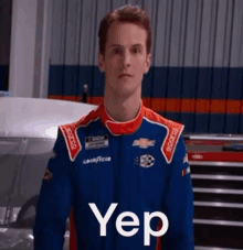 a young man in a race car suit is standing in front of a race car and says yep .