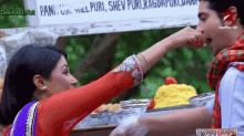 a man is feeding a woman a piece of food in front of a sign that says " pant "